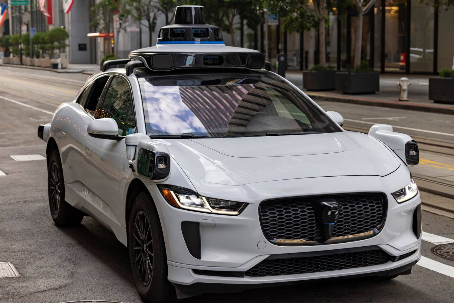 A white self-driving robotaxi with roof-mounted sensors on a city street